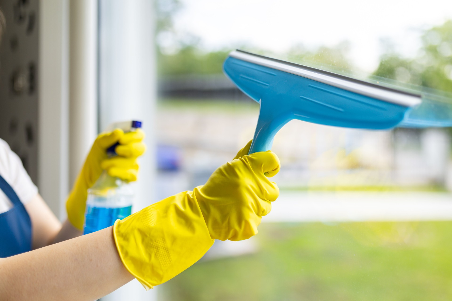 Person cleaning a window with a squeegee and spray cleaner in a bright setting